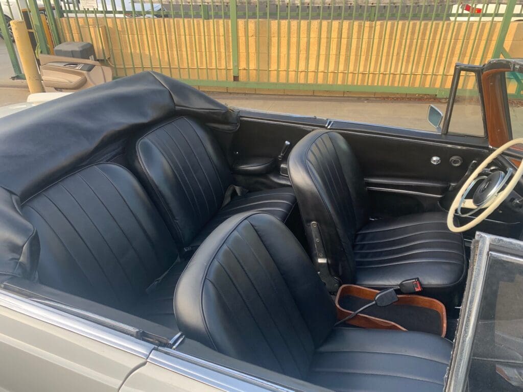 Interior view of a classic car with black leather seats and a wooden steering wheel.