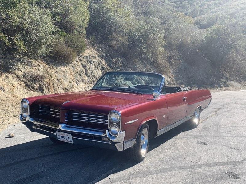 Classic red convertible car parked on a sunny hillside road.