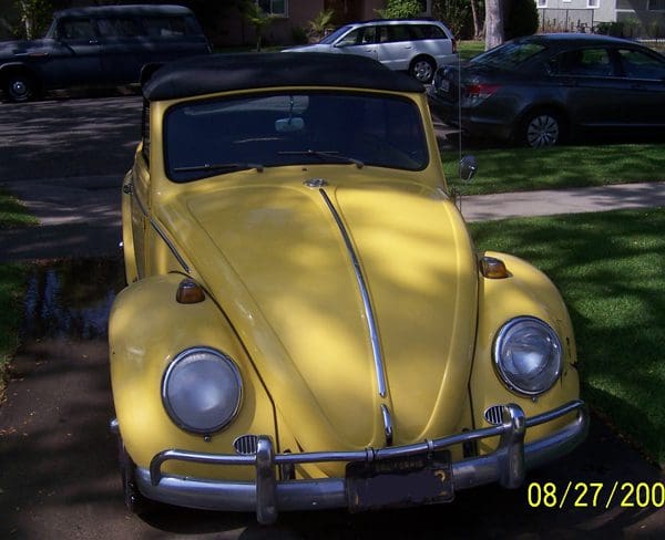 A classic yellow Volkswagen Beetle parked in a shaded area.
