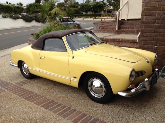 Classic yellow convertible car parked by a waterfront home.