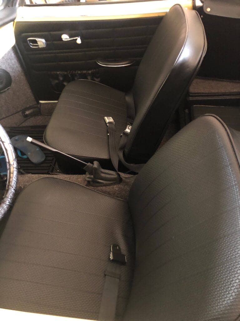 Interior view of a classic car with black cloth seats and manual gear shift.
