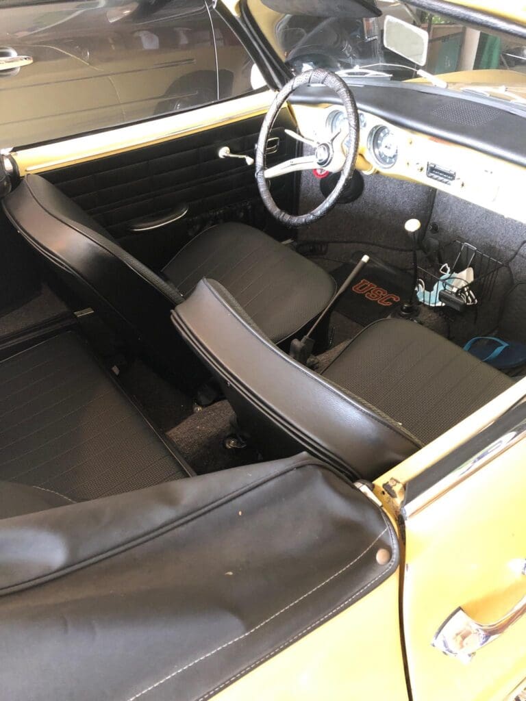 Interior view of a vintage car with black leather seats and a wooden steering wheel.