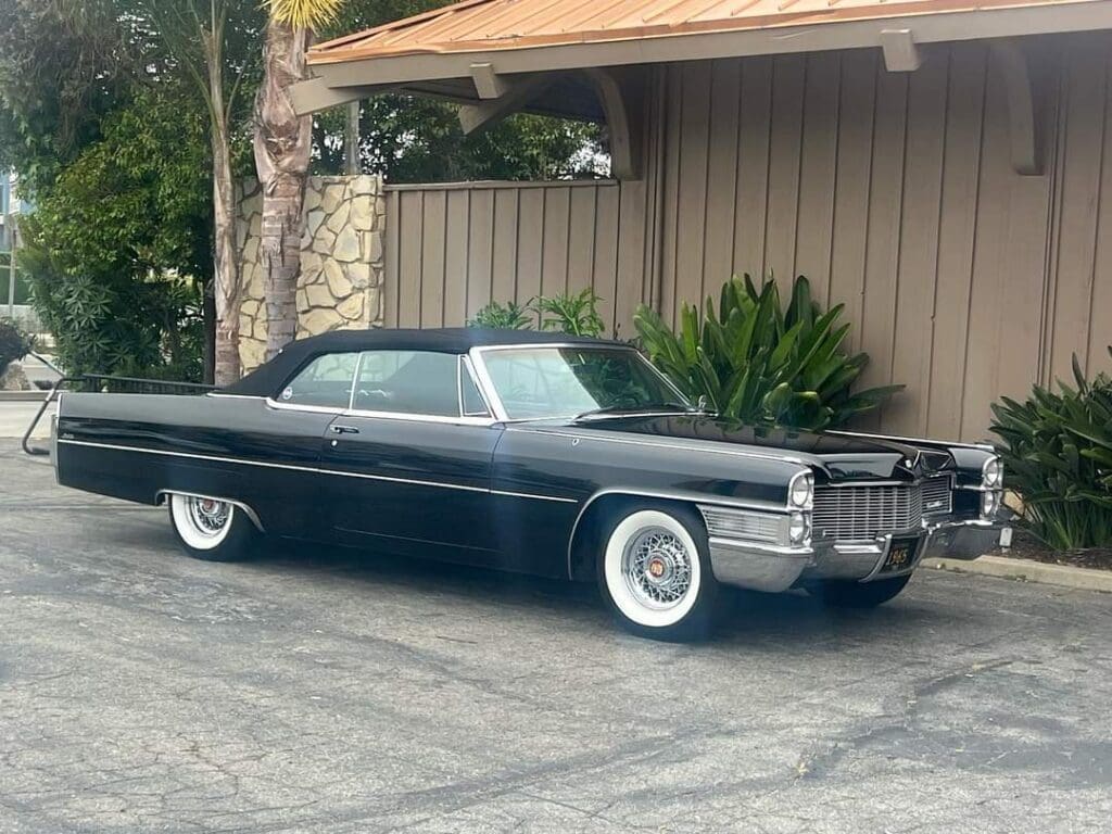 Classic black convertible car parked by a house with whitewall tires.