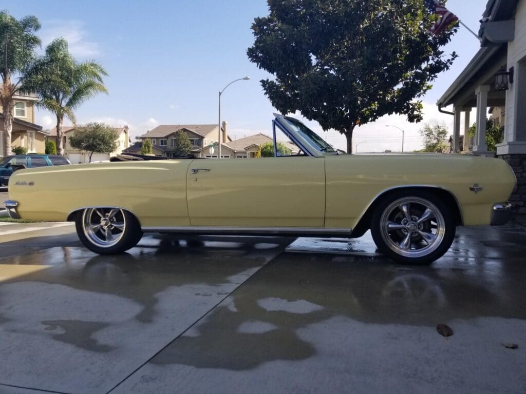 Classic yellow convertible car parked outdoors on a wet driveway.