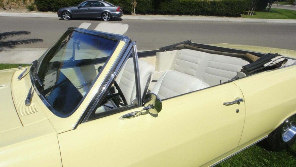 Classic yellow convertible car with white leather seats parked outdoors.