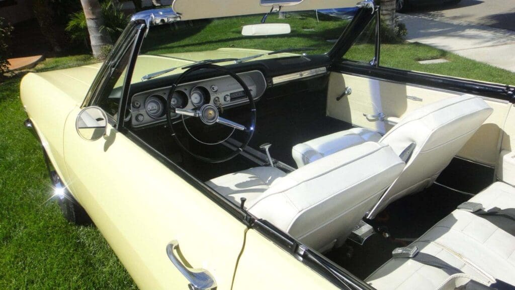 Interior of a classic convertible car with white leather seats and a black dashboard.