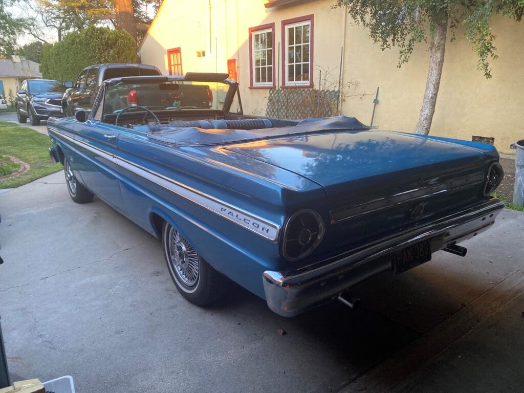 A classic blue convertible car parked near a house.