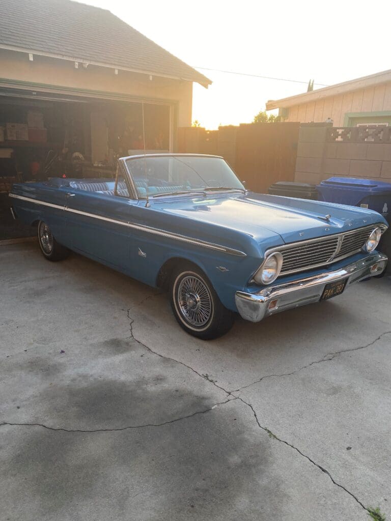 Classic blue convertible car parked in a driveway at sunset.