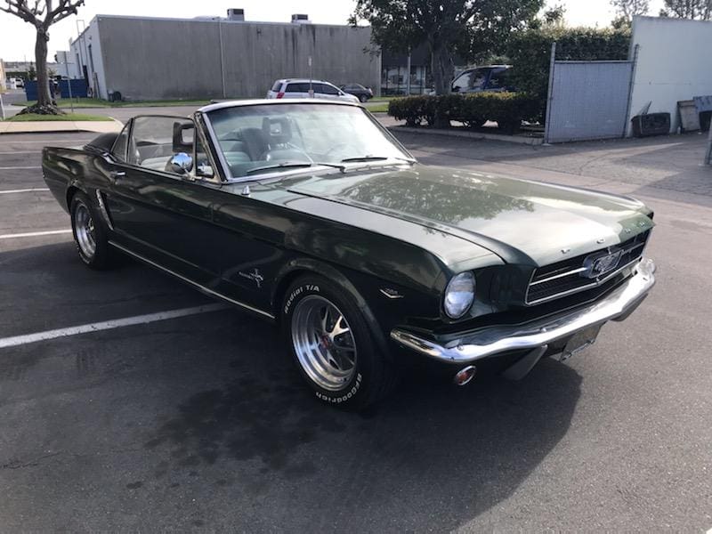 Classic black Ford Mustang convertible parked outdoors under sunlight.