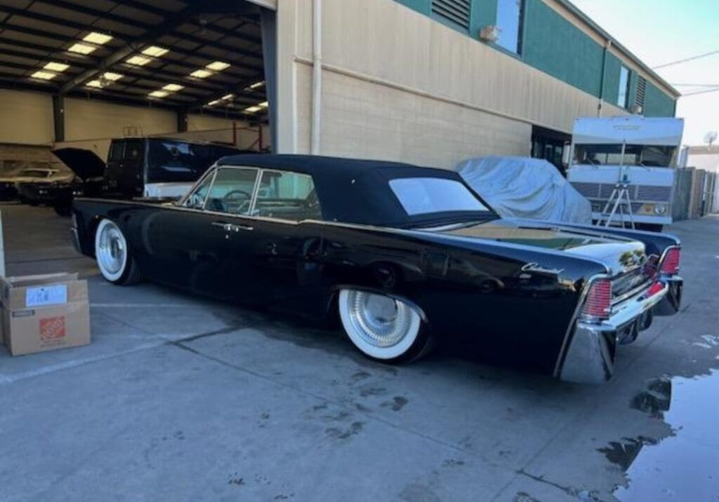 Classic black car with whitewall tires parked outside a garage.