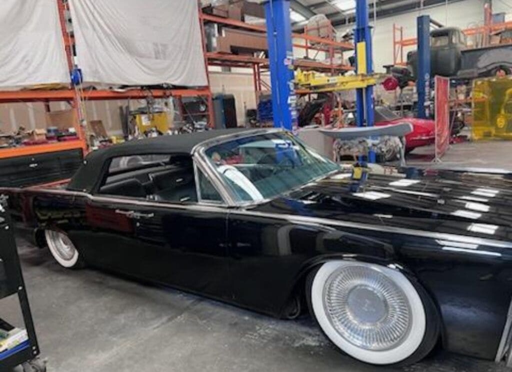 Classic black car with whitewall tires in a workshop.