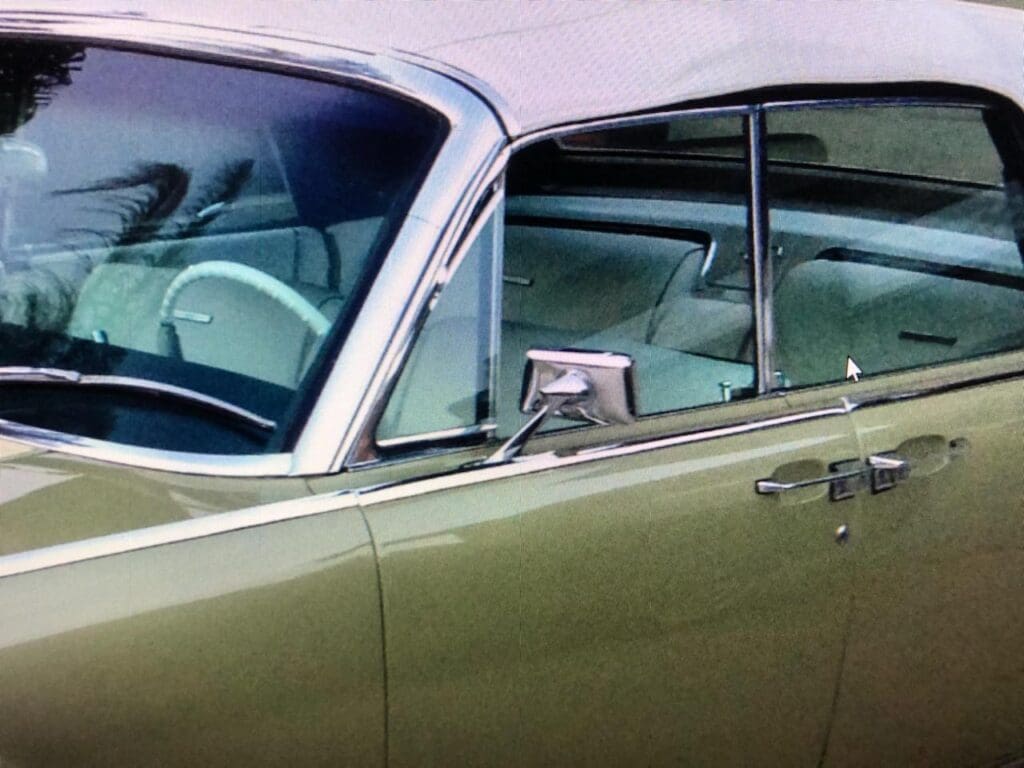 Close-up of a vintage car's side window and door in metallic green.