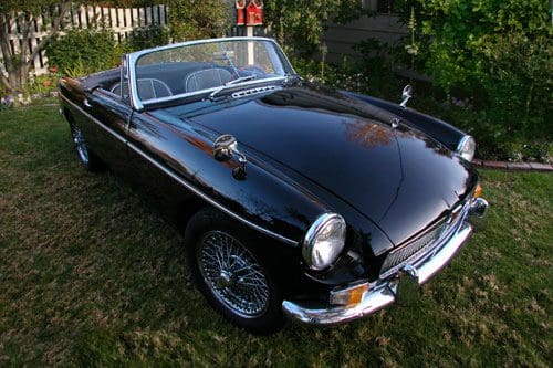 Classic black convertible sports car parked on grass.