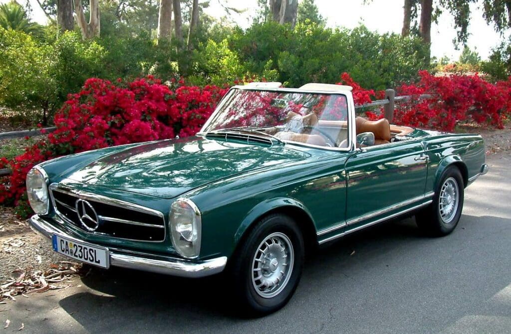 Classic green Mercedes convertible parked with red flowers in background.
