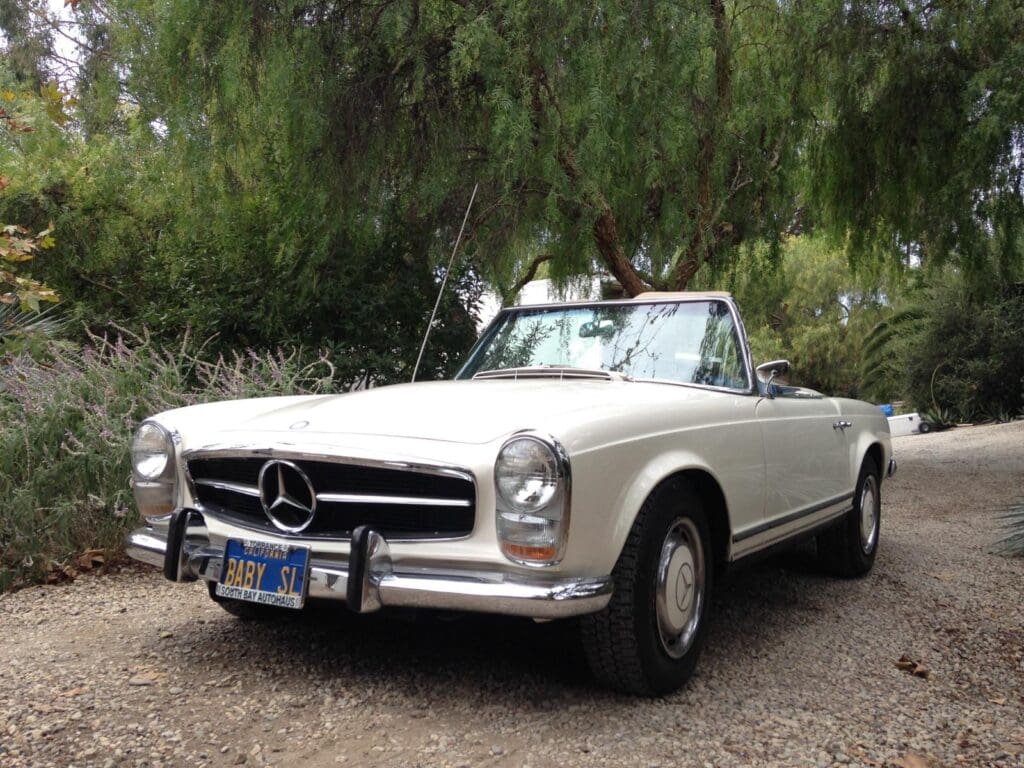 Classic white Mercedes convertible parked on a gravel path.
