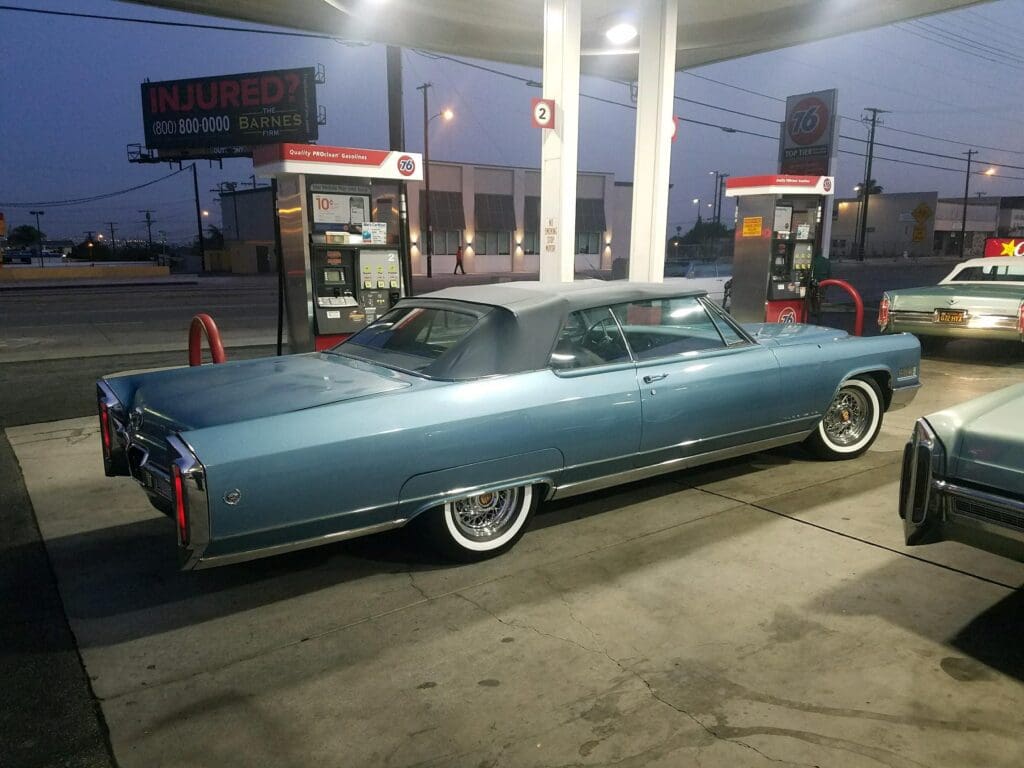 Classic blue vintage car at a gas station at dusk.
