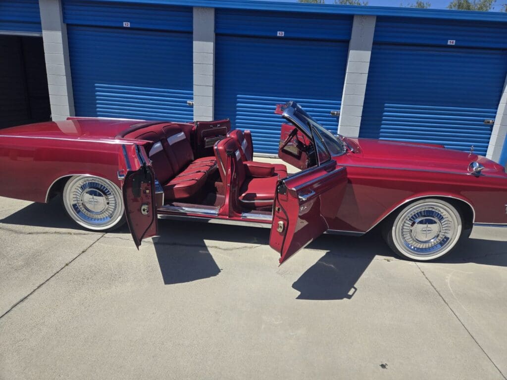 Classic red convertible car with doors and roof open, parked outside blue garage doors.