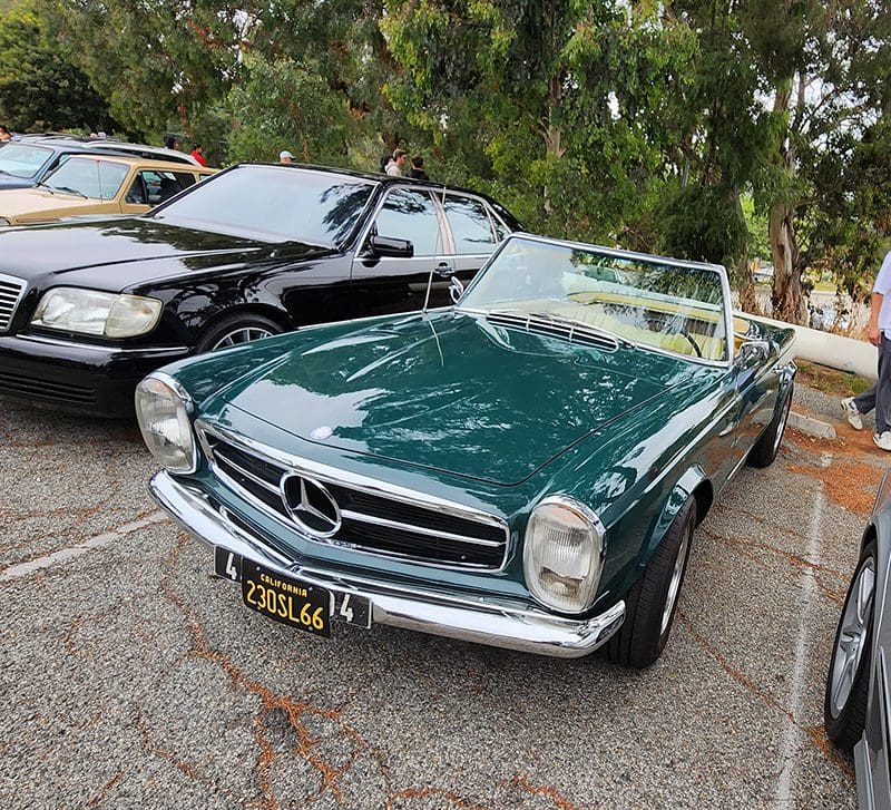 Classic green Mercedes convertible parked outdoors among other cars.