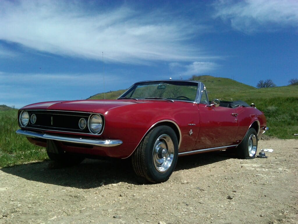Red classic convertible car parked on a dirt path under a blue sky.
