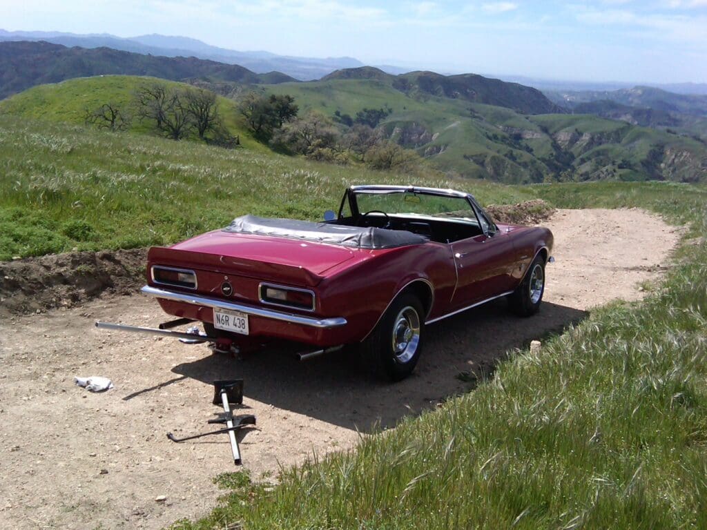 Classic red convertible parked on a scenic hill with rolling green landscapes.