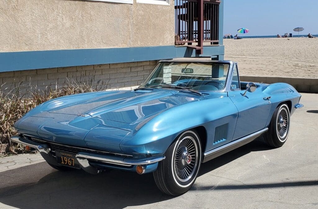 A classic blue convertible sports car parked by a building near the beach.