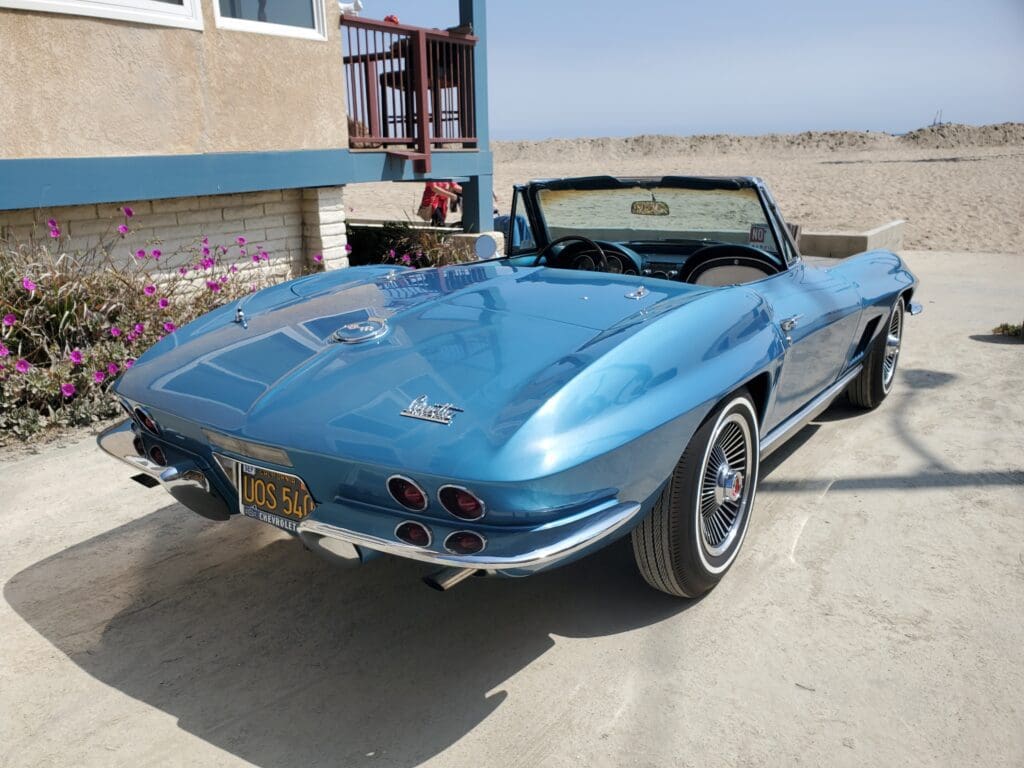 A classic blue convertible parked near a beach house.