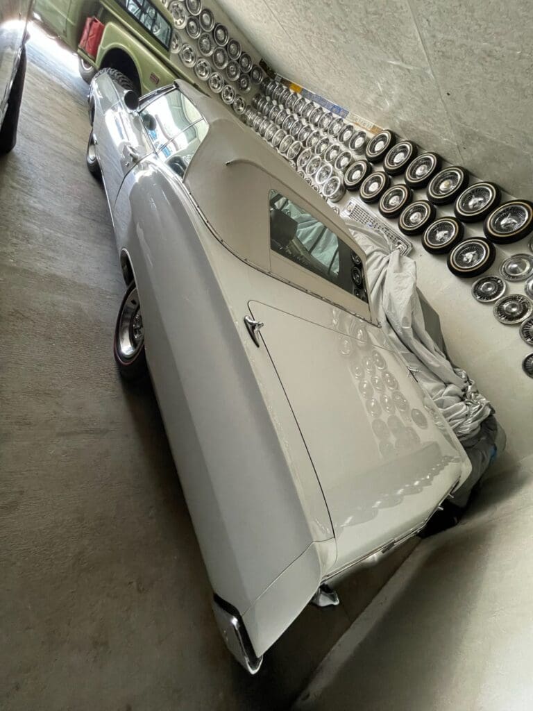 Classic white car parked indoors next to a row of tires.