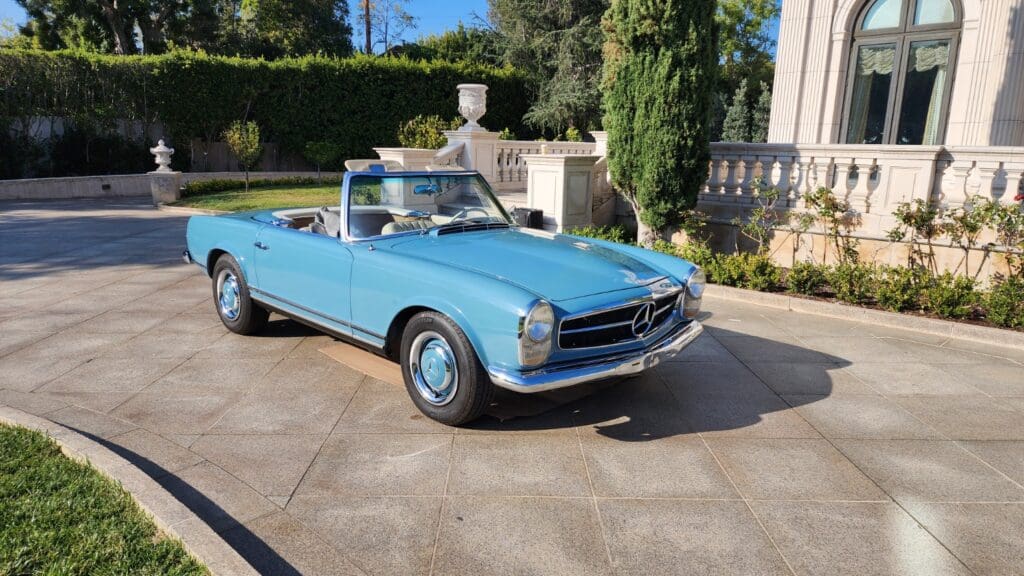 Classic light blue convertible car parked on driveway under the sun.