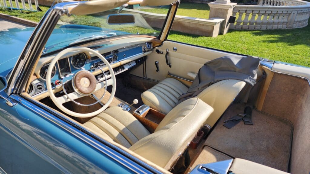 Interior of a vintage convertible car with beige leather seats and a classic steering wheel.