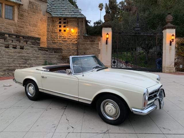 Classic white convertible car parked on a stone driveway.