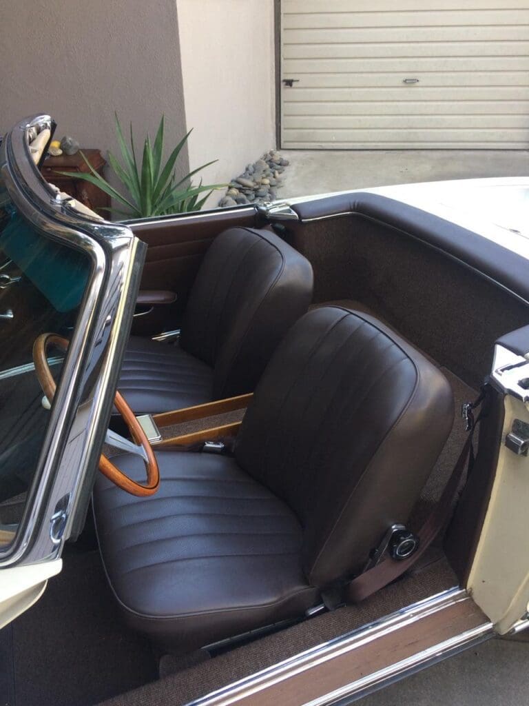 Interior view of a classic convertible car with black leather seats and wooden steering wheel.