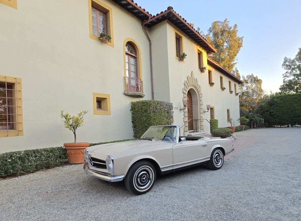Classic white convertible car parked in front of a Mediterranean-style house.