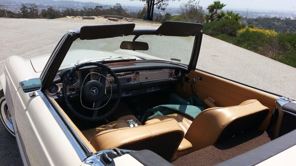 Interior of a classic convertible car with tan leather seats and a scenic ocean view.