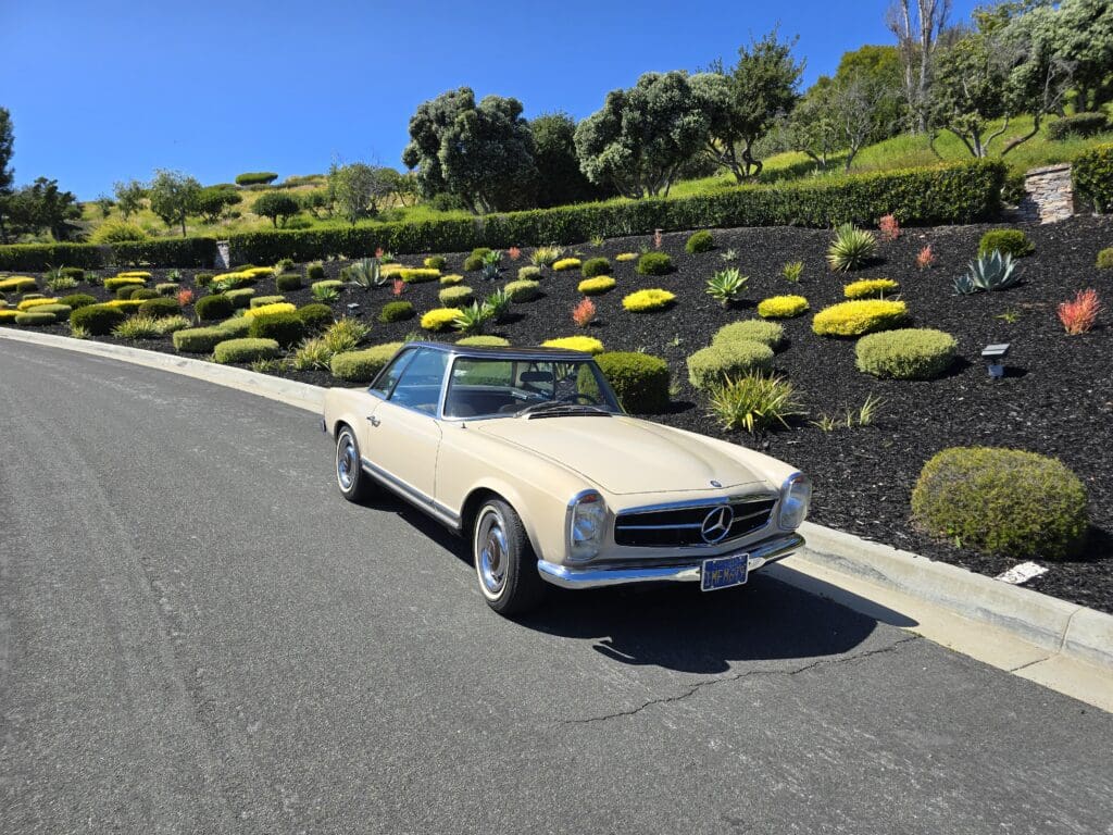 Classic white convertible car parked on a sunny road with greenery.