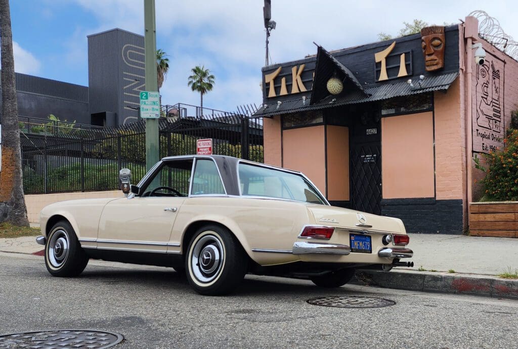 Vintage cream convertible car parked near a tiki bar.