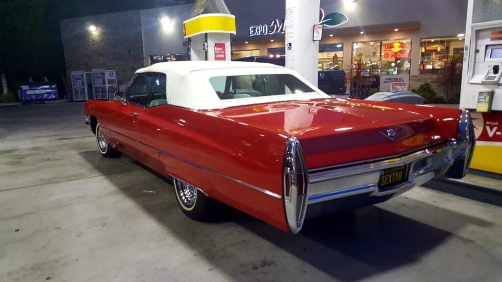 Classic red convertible car parked at a gas station at night.
