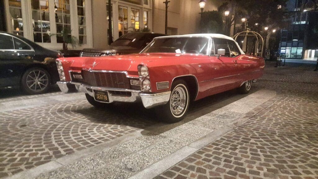 Classic red convertible car parked on a cobblestone street at night.