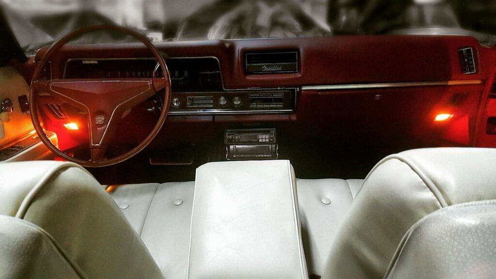 Vintage car interior with white leather seats and a wooden steering wheel.