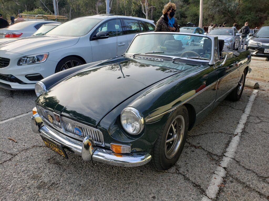 Classic black convertible car parked outdoors with people nearby.