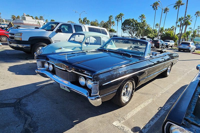 Classic black convertible car parked in a sunny lot with palm trees.