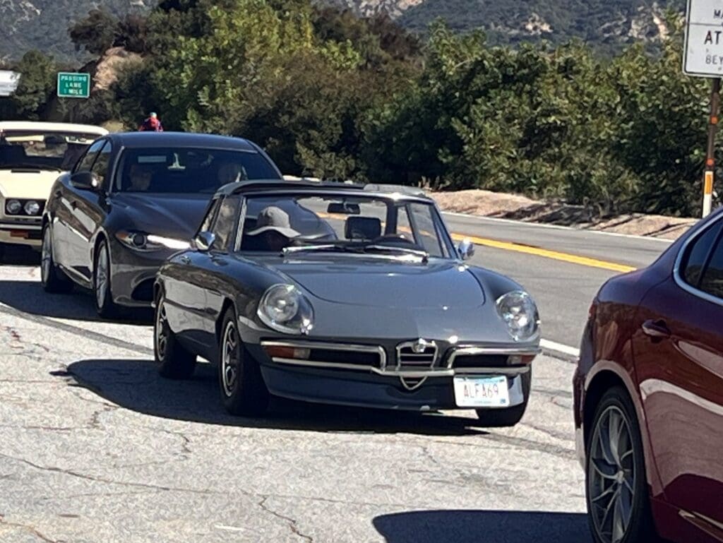 Classic silver convertible car driving on a scenic mountain road.