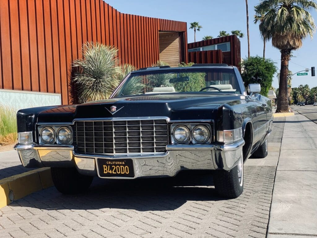 Classic black Cadillac parked on a sunny street with a wooden building backdrop.