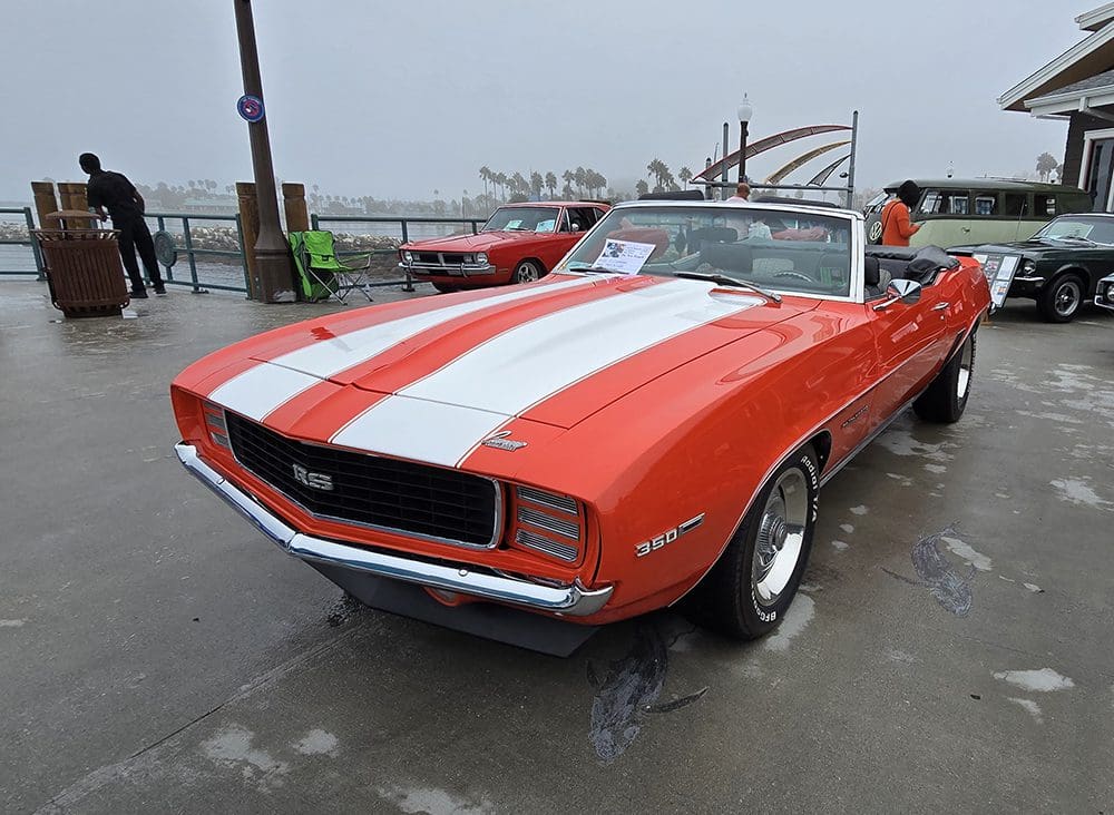 Classic red and white-striped convertible car parked near a dock.