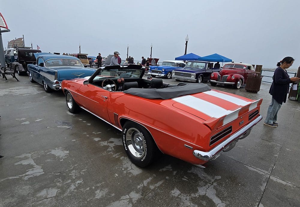 Classic red and white-striped convertible car parked near a dock.