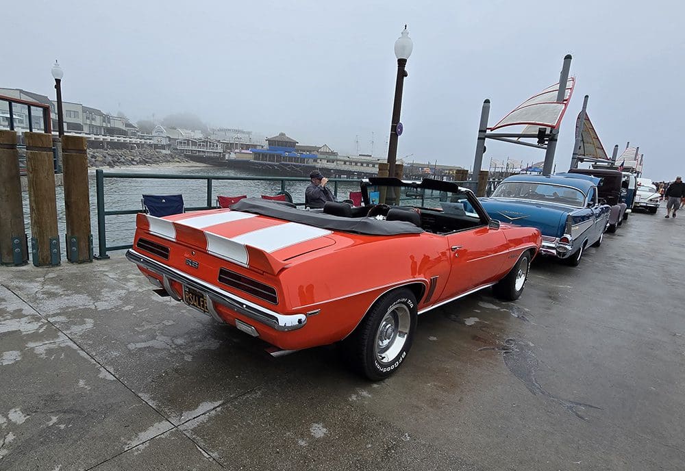 Classic red convertible parked by the waterfront on a gray day.