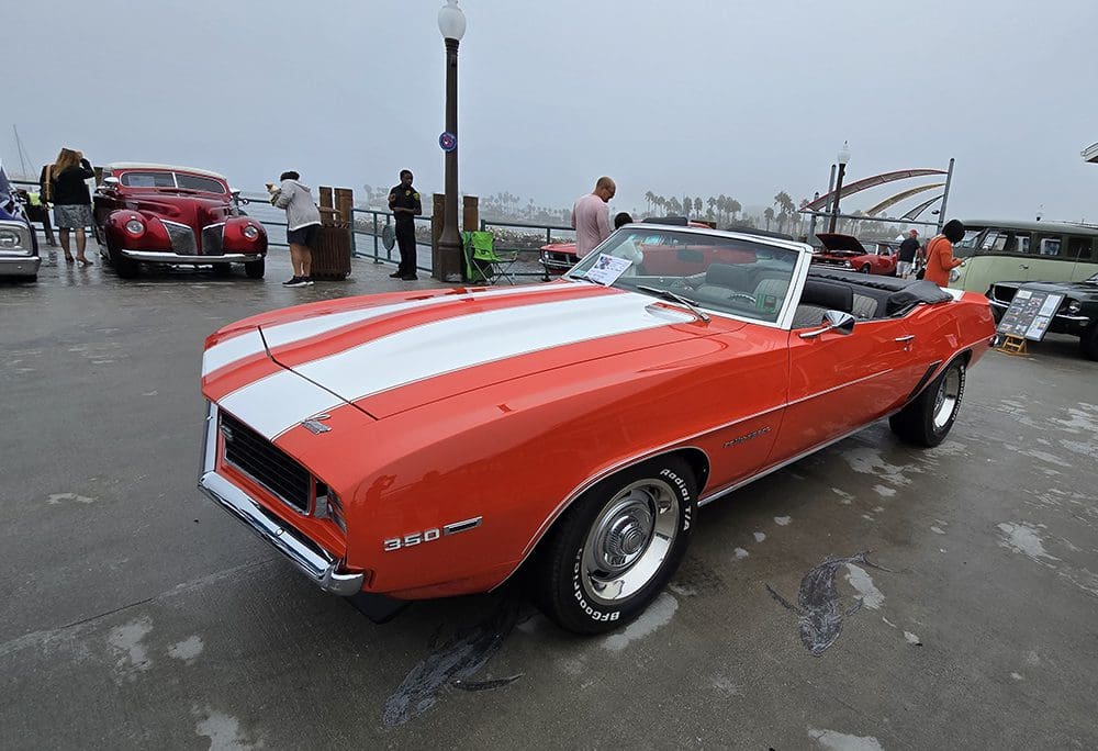 Classic orange convertible car with white racing stripes parked on a wet street.