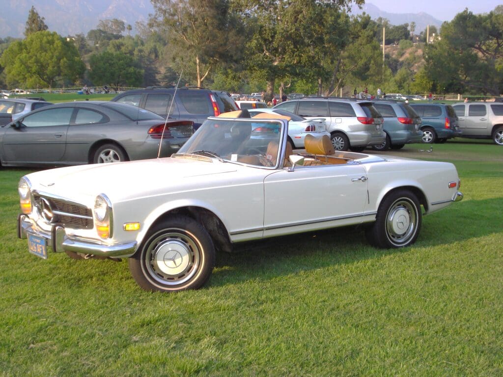 Classic white convertible car parked on the grass with a scenic background.