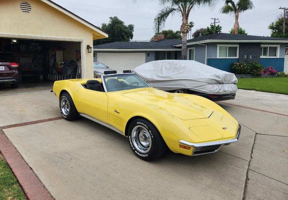 Yellow classic convertible car parked in a driveway beside a covered car.