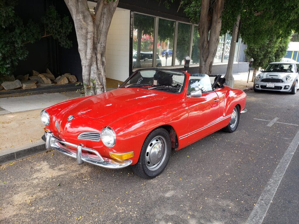 Classic red convertible parked by a tree on a sunny day.