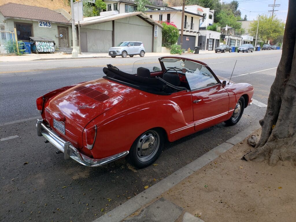 Classic red convertible car parked on a street under shade.